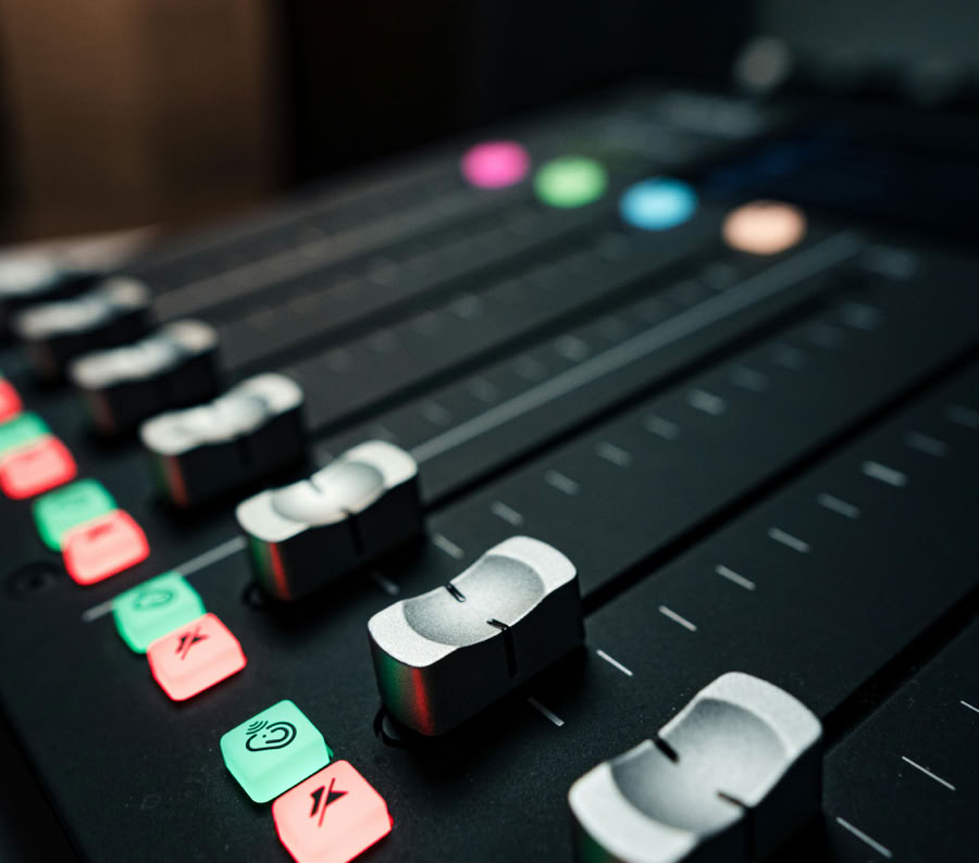 Close-up of a professional audio mixing console with sliders and illuminated control buttons.