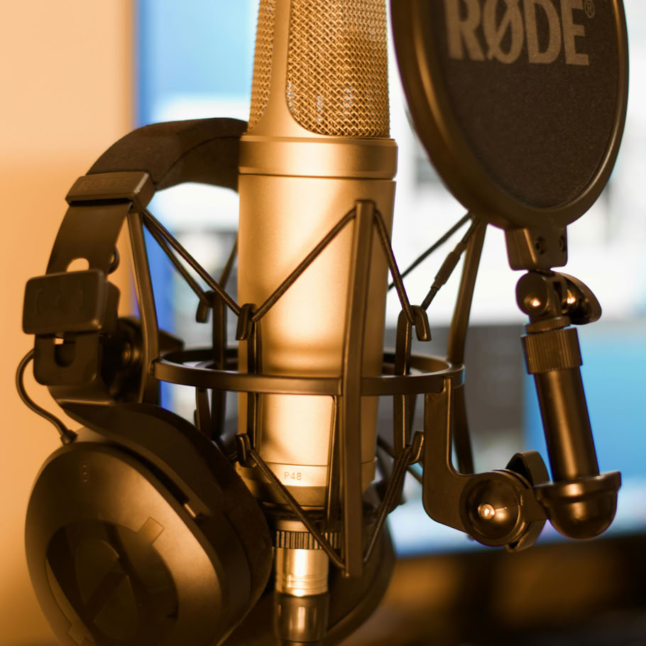 Close-up of a condenser microphone and headphones in a recording studio with soft lighting.